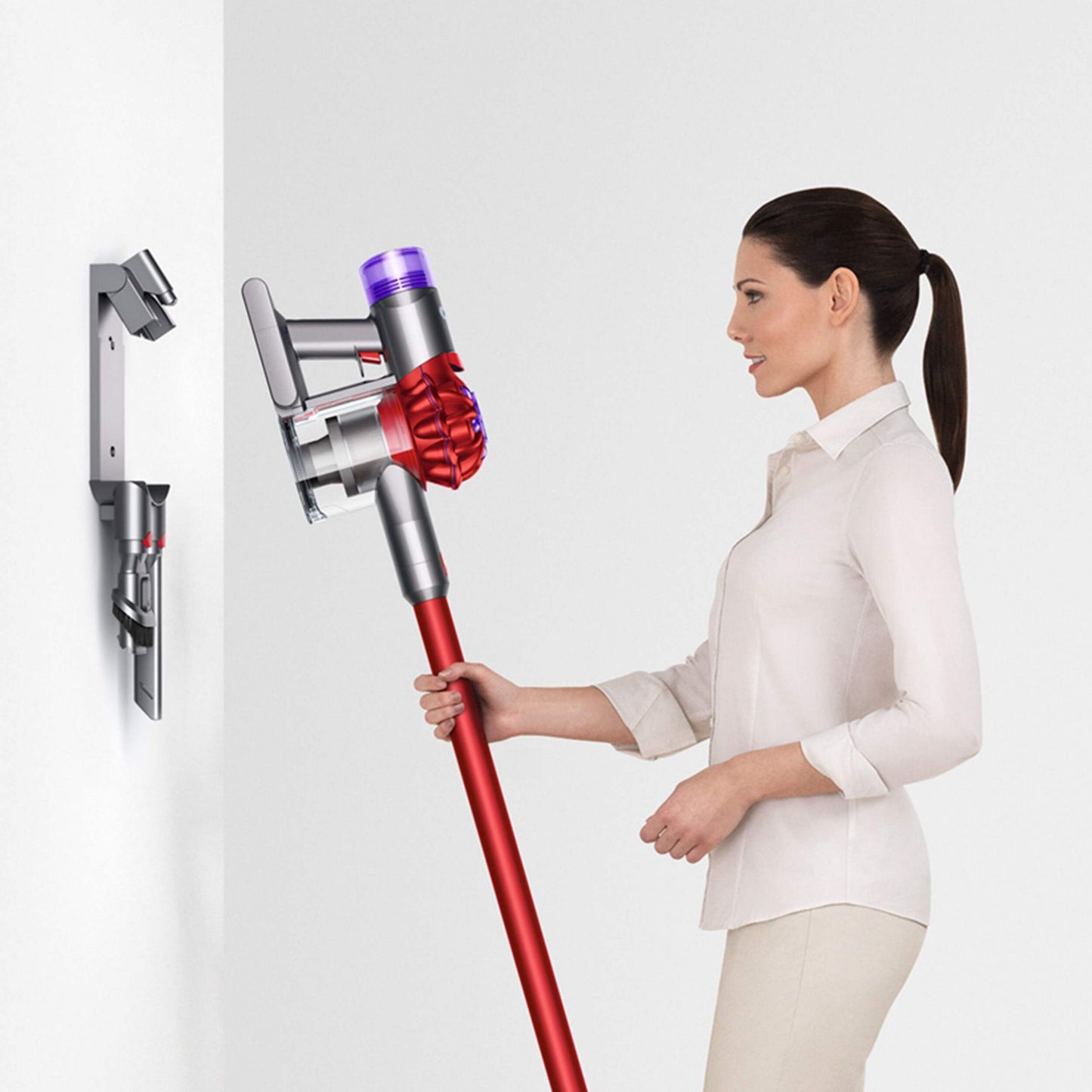 Girl putting Dyson V8 Origin in charging dock hanging on wall