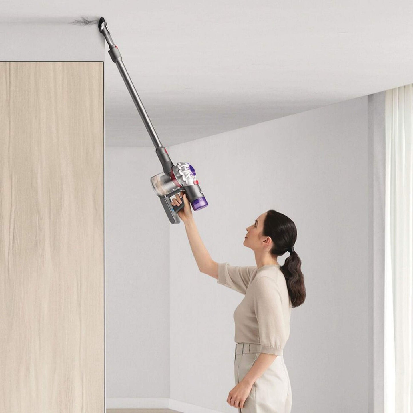Lifestyle. Girl Vacuuming ceiling with Dyson V8 Origin using the combination tool.